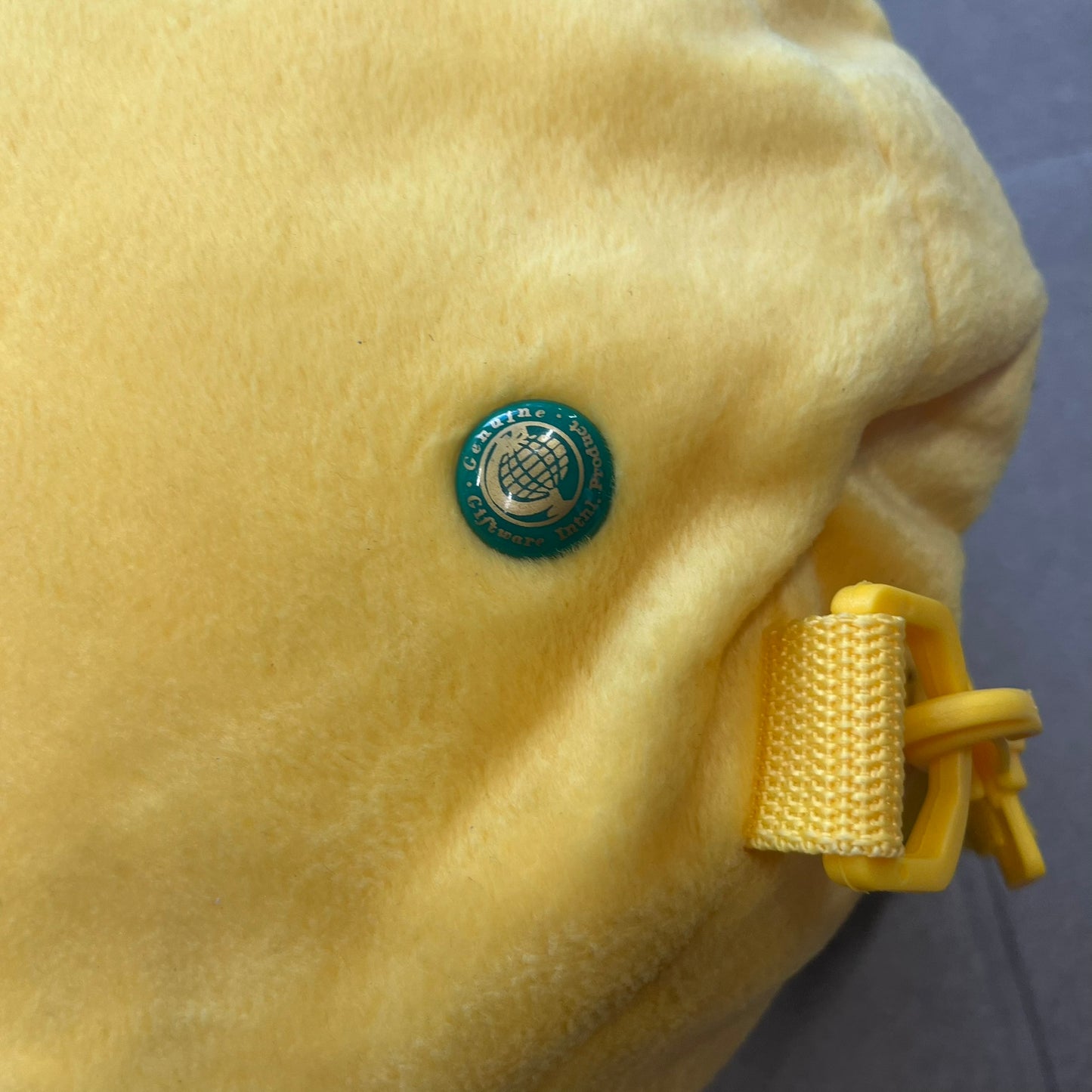 The Simpsons 1990s Homer Simpson Head Backpack is a novelty backpack shaped like a 3D Homer Simpson head. The design is fully yellow with soft sculpted facial features including eyes and nose, a molded mouth, and protruding ears. The hair detail wraps around the back, with the top strands functioning as a hanger. It includes yellow shoulder straps and a single main compartment.