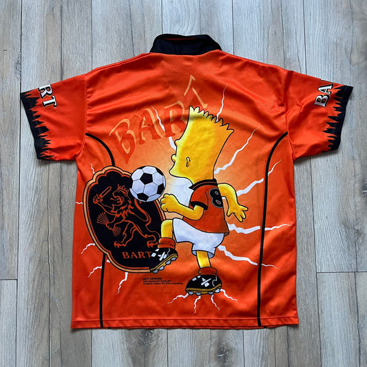 Officially licensed 1999 The Simpsons World Cup Netherlands Tee. Orange lightweight polyester tee with an all-over graphic design. The front features Bart Simpson kicking a football, orange “Bart” text, white lightning graphics, and a Netherlands emblem with Bart illustrated beneath it. Black flame details on the sleeve, along with a black ribbed collar with orange lining. Matt Groening / The Simpsons ©1999 licensing is printed below the main graphic. The back repeats the design in a flipped layout, showing