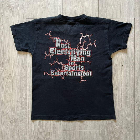 The Rock “Most Electrifying Man” 2000 Tee is a vintage WWE shirt featuring bold metallic-textured lettering with red lightning accents. The front proudly displays “The Rock,” while the back proclaims “The Most Electrifying Man in Sports Entertainment.” Licensed by World Wrestling Federation (WWF), this 2000 release is a must-have collectible for wrestling fans!