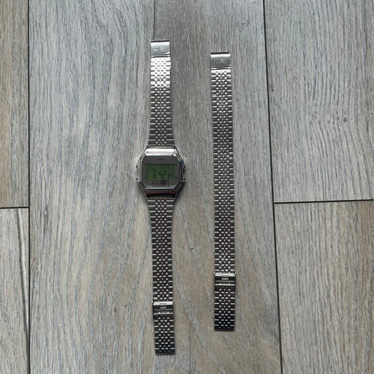 Timex x Maison Margiela MM6 Gift Set TWG065600 is a collaborative reinterpretation of the classic Timex T80, released on October 24, 2024. Crafted from polished and brushed stainless steel, it features a 36mm digital case with Timex branding and a distinctive 0–23 numeral layout, including a subtle circled “6” nod to MM6 design language. The watch offers 100 ft water resistance, mineral glass, backlight, alarm, timer, and date functions, and is presented as a 2-in-1 gift set with an additional standalone st