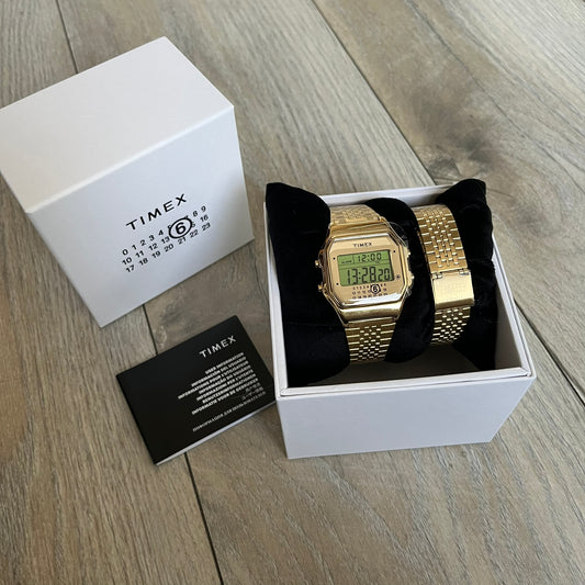 Timex x Maison Margiela MM6 Gold Watch + Bracelet Gift Set TWG067500QY is a collaborative reinterpretation of the classic Timex T80, released on October 24, 2024. Crafted from polished and brushed stainless steel, it features a 36mm digital case with Timex branding and a distinctive 0–23 numeral layout, including a subtle circled “6” nod to MM6 design language. The watch offers 100 ft water resistance, mineral glass, backlight, alarm, timer, and date functions, and is presented as a 2-in-1 gift set with an