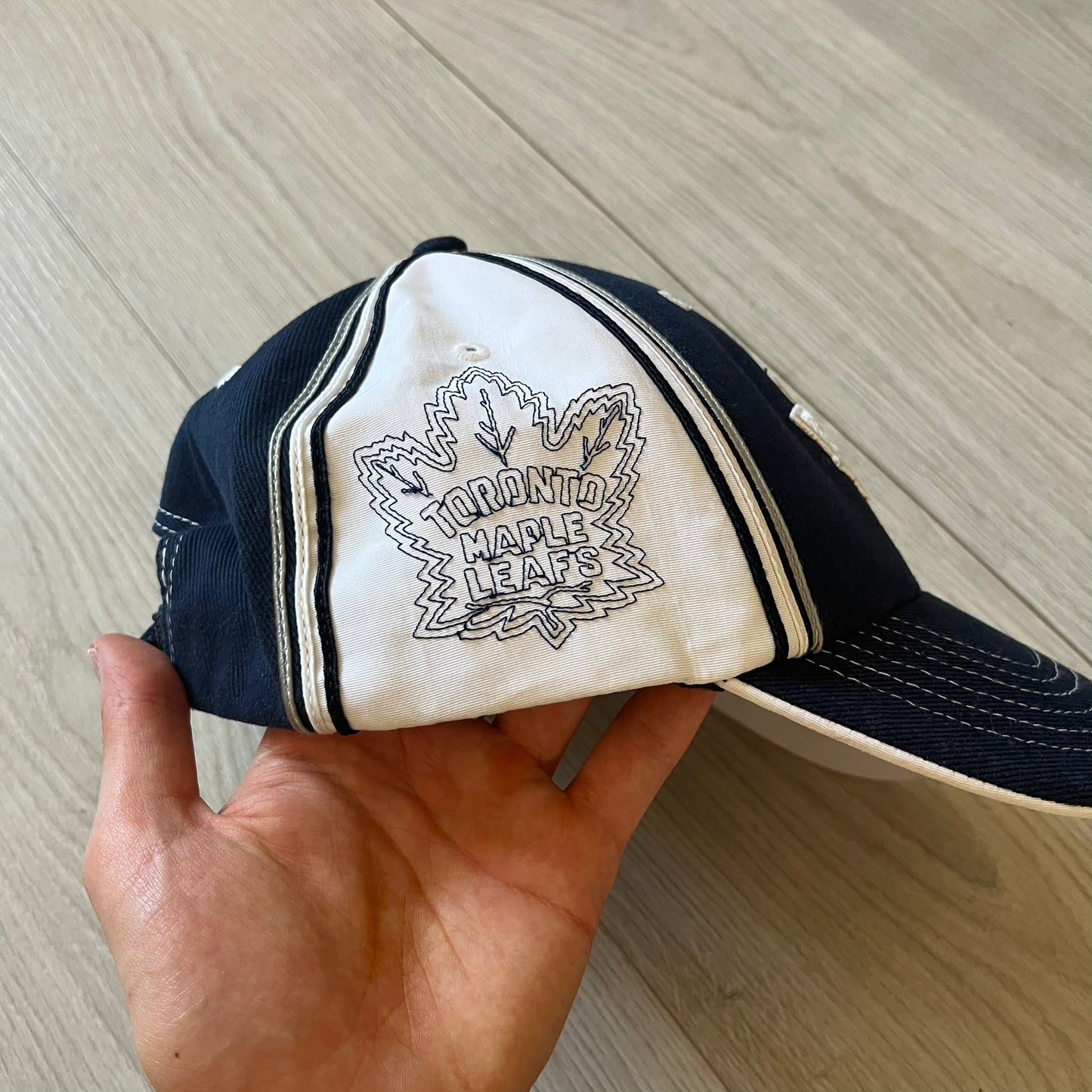 Hand holding a blue and white cap with 'Toronto Maple Leafs' logo on a wooden surface