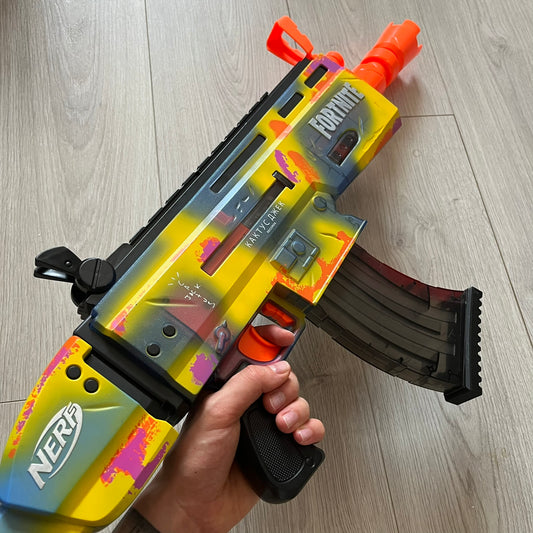 Hand holding a colorful Nerf gun on a wooden floor