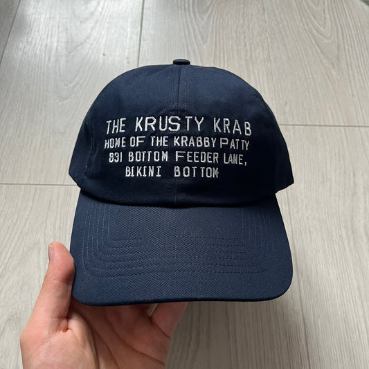 Uniqlo x CPFM Spongebob Navy Cap from FW24, released on 12/12/2024. This navy UV protection cap features a playful SpongeBob SquarePants design, part of the Uniqlo x Cactus Plant Flea Market collaboration. Lightweight and functional, it combines casual style with sun protection, making it a fun and practical accessory.