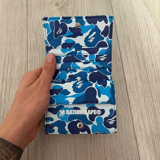 Blue camouflage wallet with a brand logo held by a hand on a wooden surface