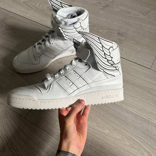 The Adidas Jeremy Scott Wings 4.0 Forum Hi launched on May 5, 2022, in a white and black colorway. Premium leather uppers highlight black stripes, heel tab, and Wings branding, while the high-top structure provides support with a padded collar and tongue. Equipped with a rubber herringbone outsole for grip, this limited edition release merges classic silhouette with JS design.