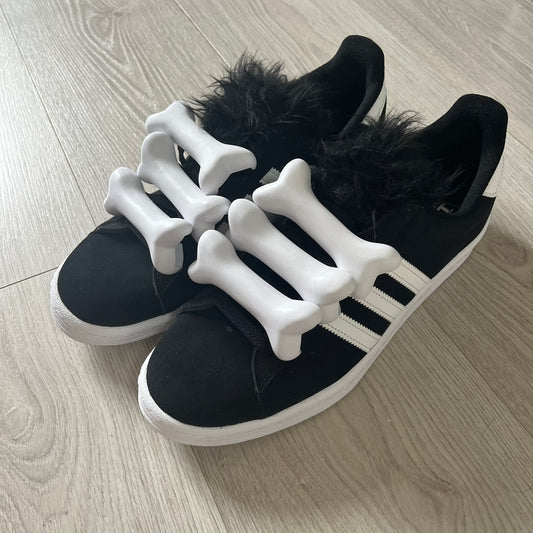 jeremy scott’s take on the adidas campus 80s includes black leather, serrated stripes, and unique faux fur tongues. detachable white bones on the laces add a customizable, standout touch. this 2023 release balances classic style with avant-garde details.
