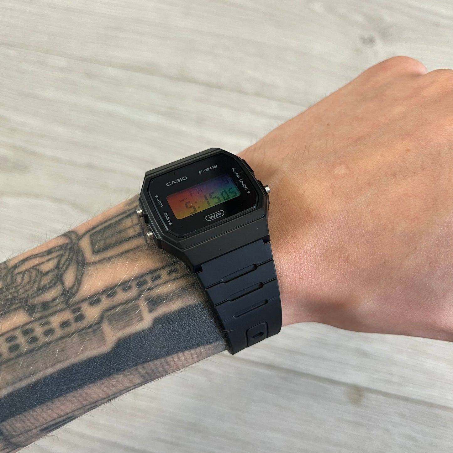 Black Casio watch on a wrist with tattoos, against a light background