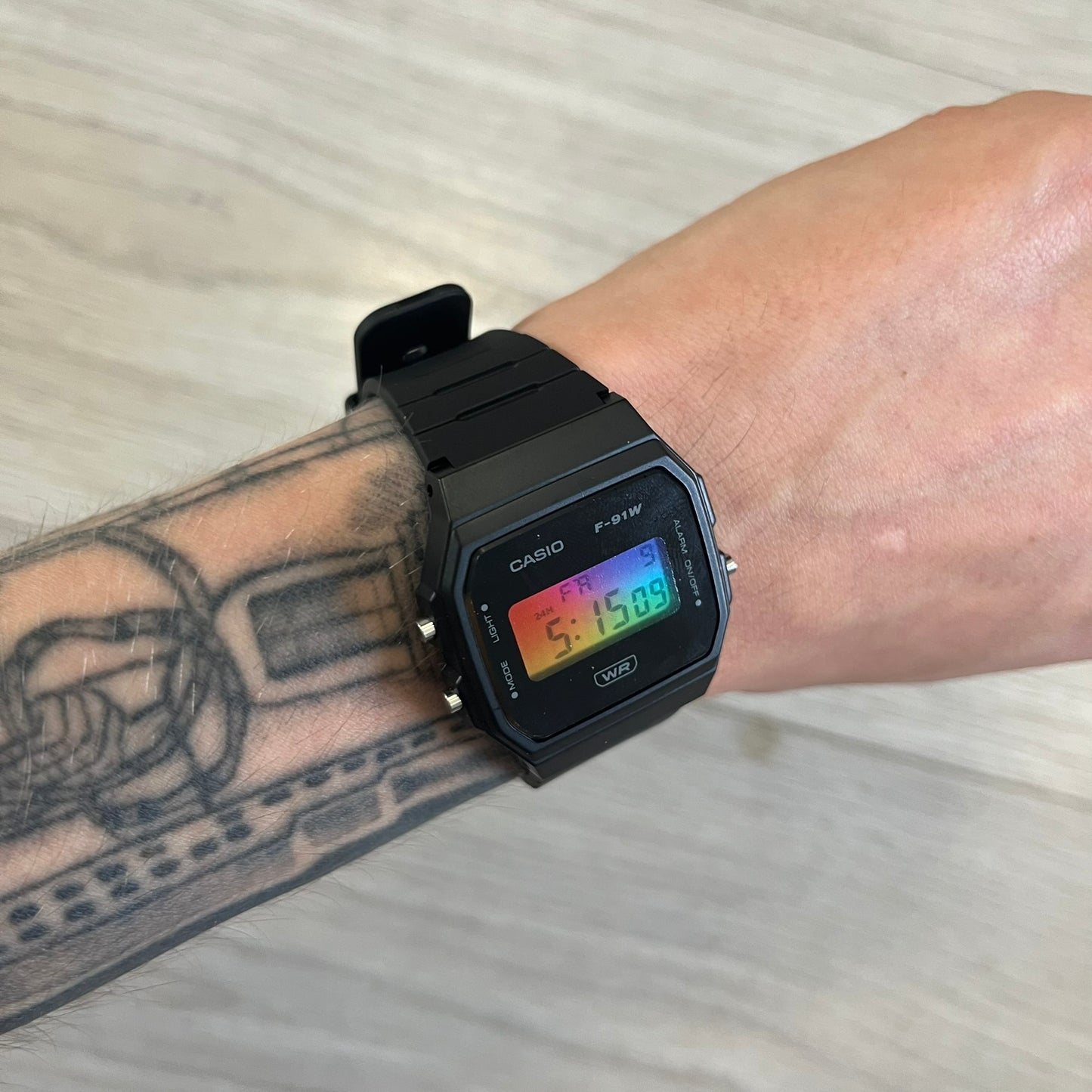 Black Casio digital watch on a wrist with tattoos, on a light background