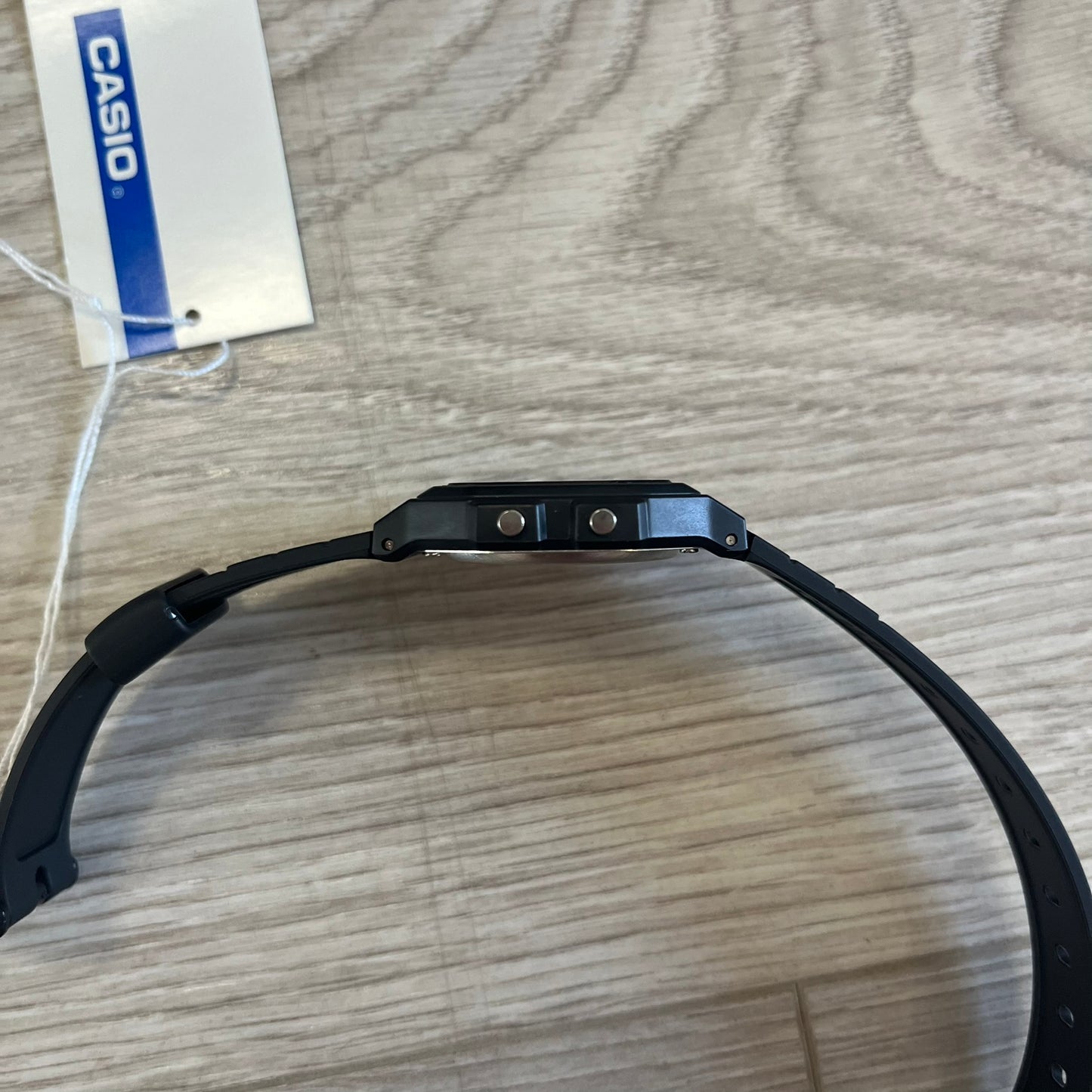 Black Casio watch band on a wooden surface with a visible Casio tag.