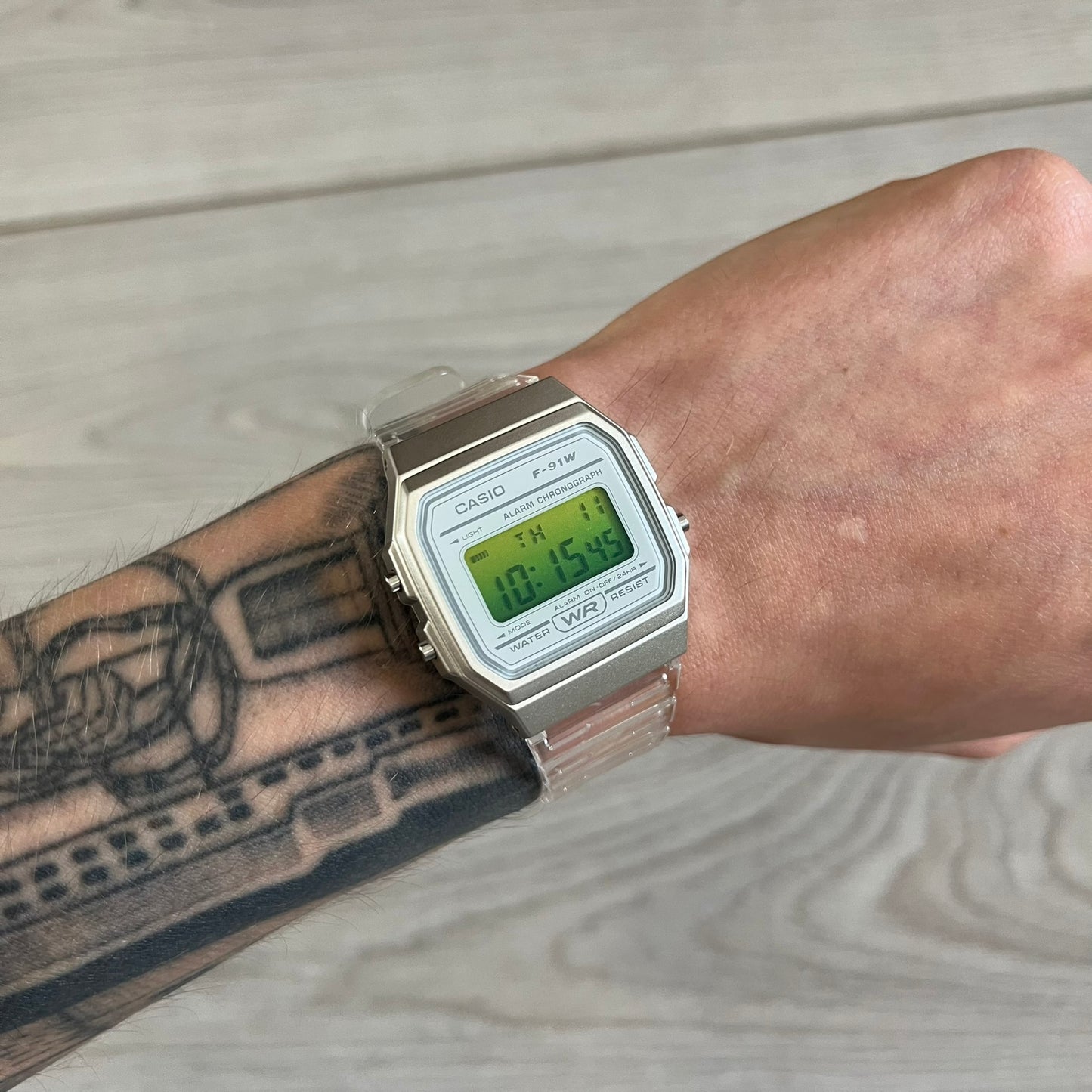 Digital watch on a wrist with tattoos, on a wooden surface