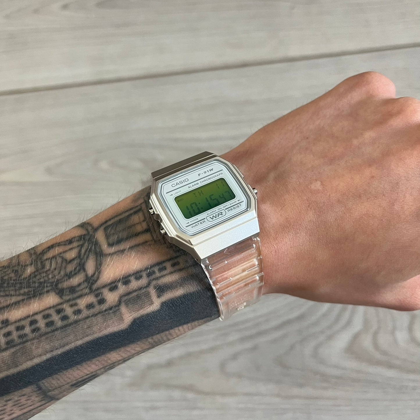 Digital watch on a wrist with tattoos against a wooden background