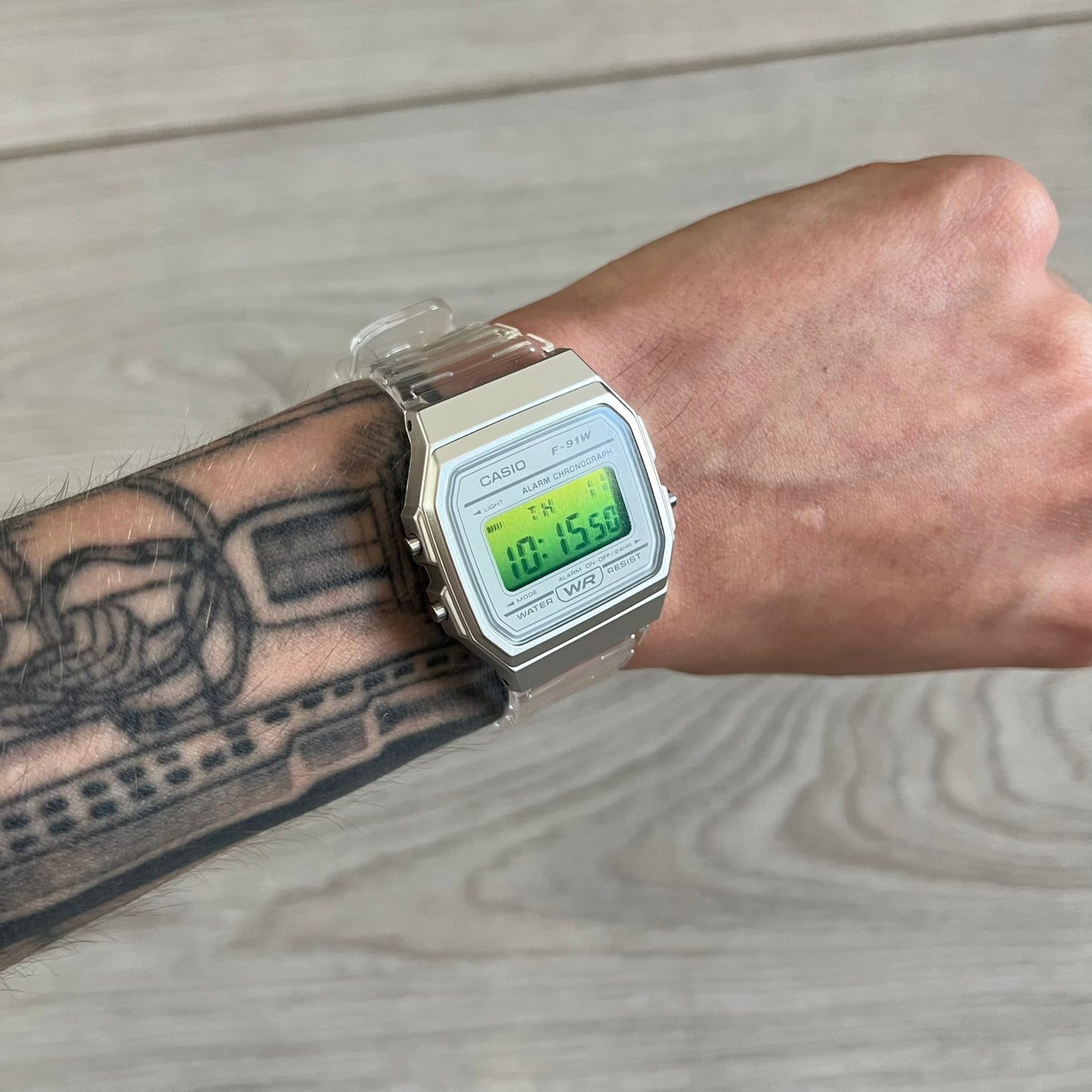 Digital watch on a wrist with a tattooed arm, wooden surface background