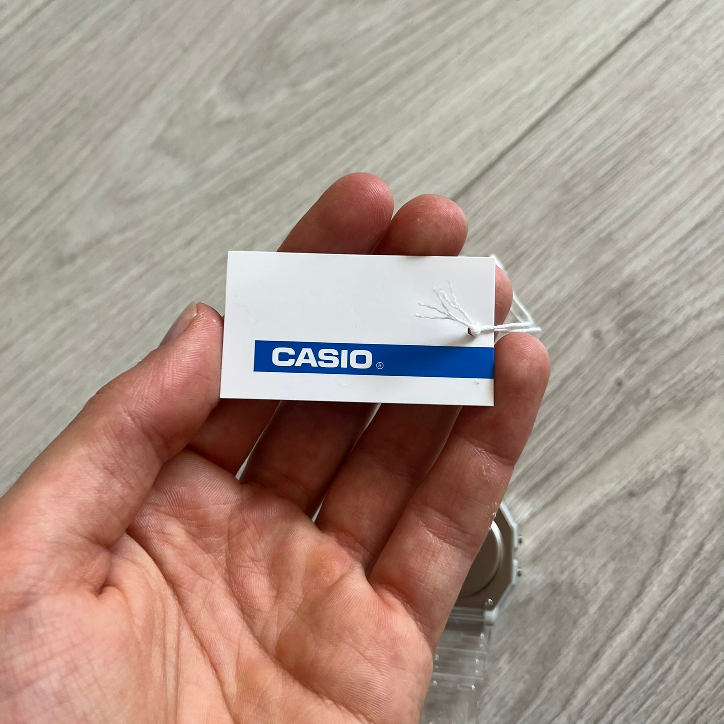 Hand holding a Casio tag against a wooden surface