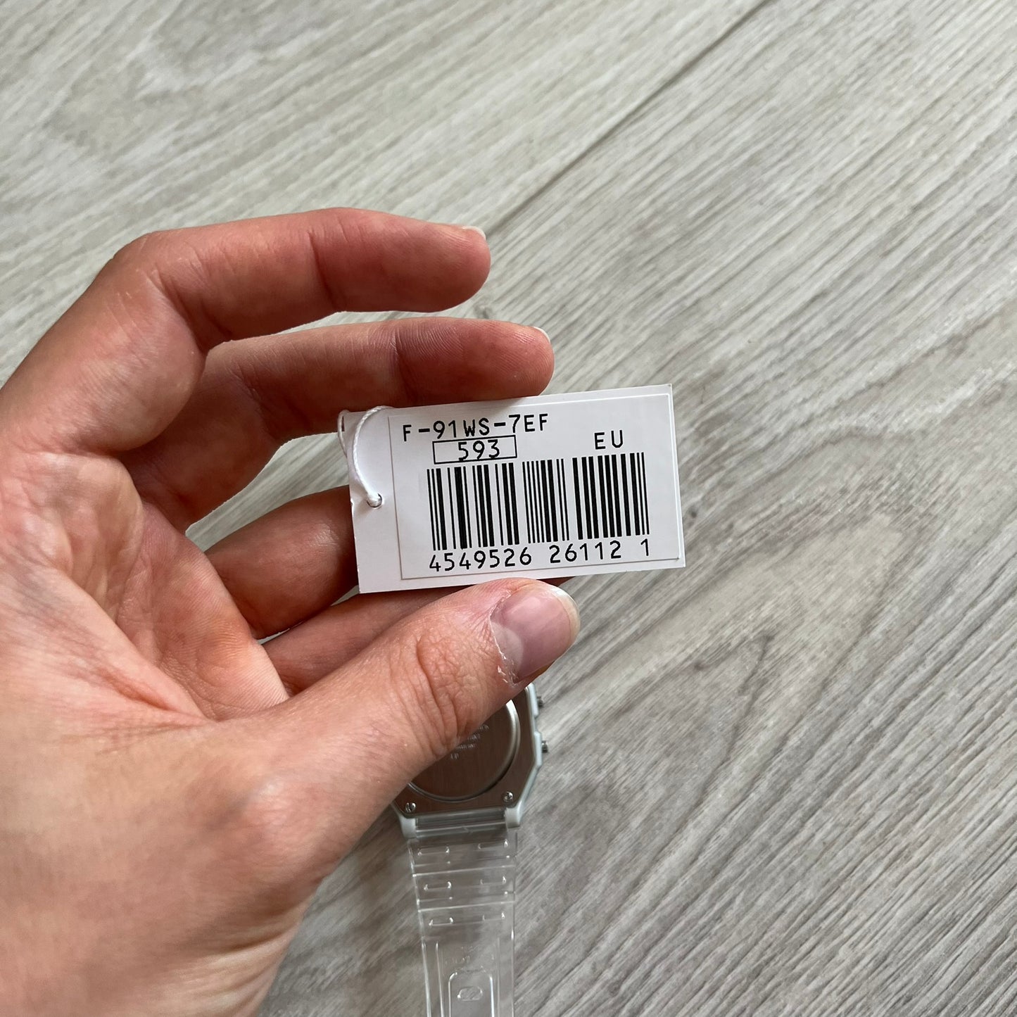 Hand holding a small white label with a barcode on a gray surface