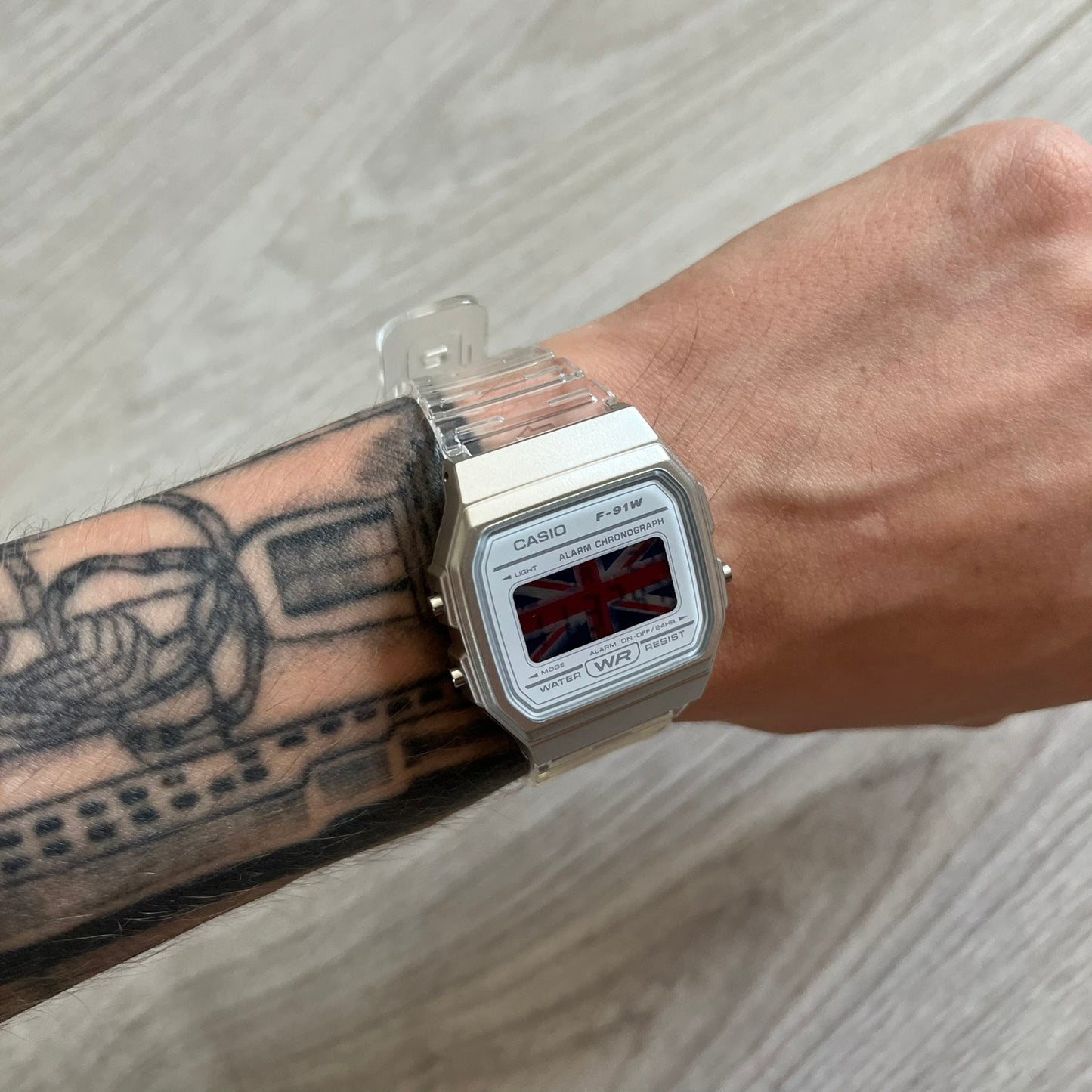 Casio digital watch with a Union Jack display on a wrist with tattoos.