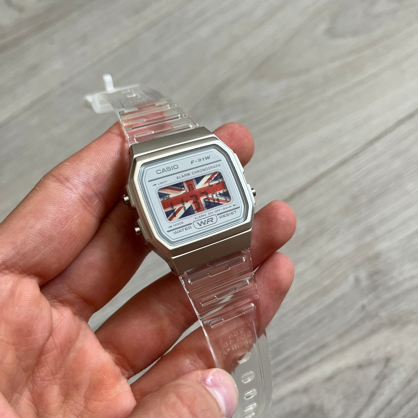 Casio watch with a clear strap held in a hand on a gray surface