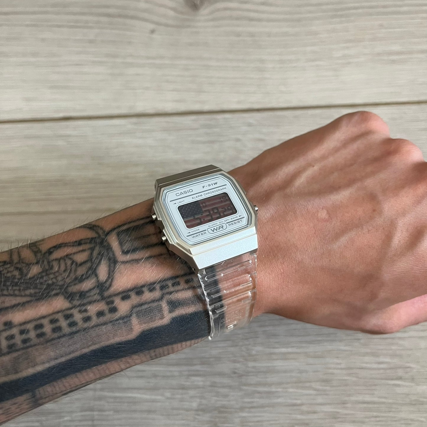 Person wearing a silver Casio watch on a wooden surface