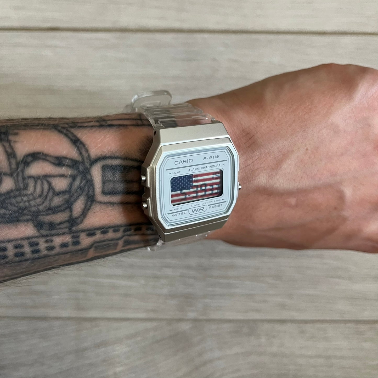 Casio watch with American flag display on a wrist with tattoos, on a wooden surface