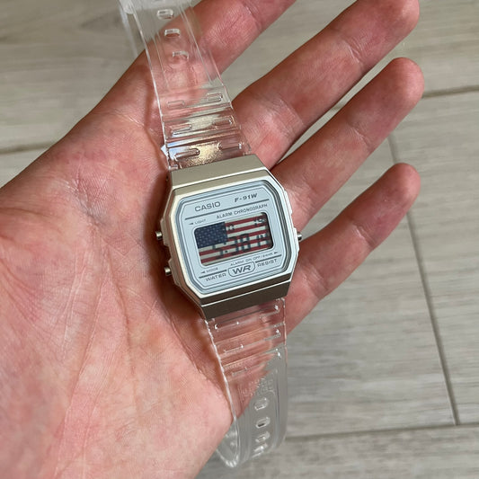 Custom Casio F-91W Clear/Transparent digital watch featuring a United States Flag filter screen. Slim 8.5 mm profile, lightweight 21 g build and flexible bio-based resin band ensure lasting comfort. Includes alarm, stopwatch, and microlight function for everyday functionality.
