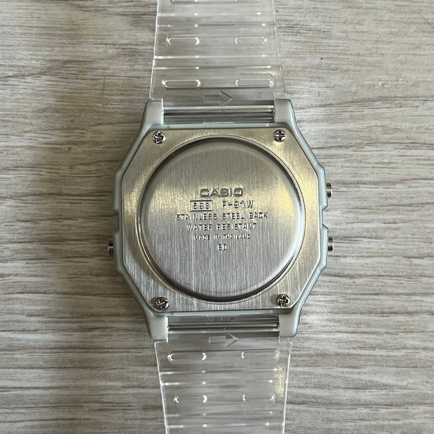 Silver Casio watch with clear plastic strap on a wooden surface