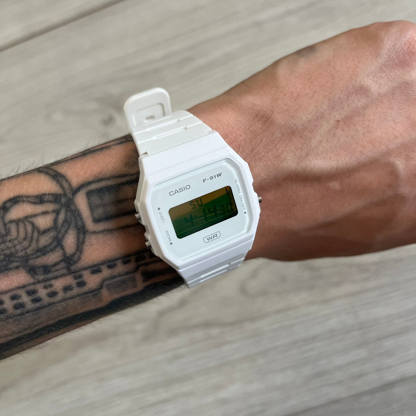 White Casio digital watch on a wrist with tattoos, on a wooden surface