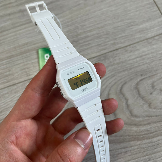 White Casio digital watch held in a hand on a wooden surface