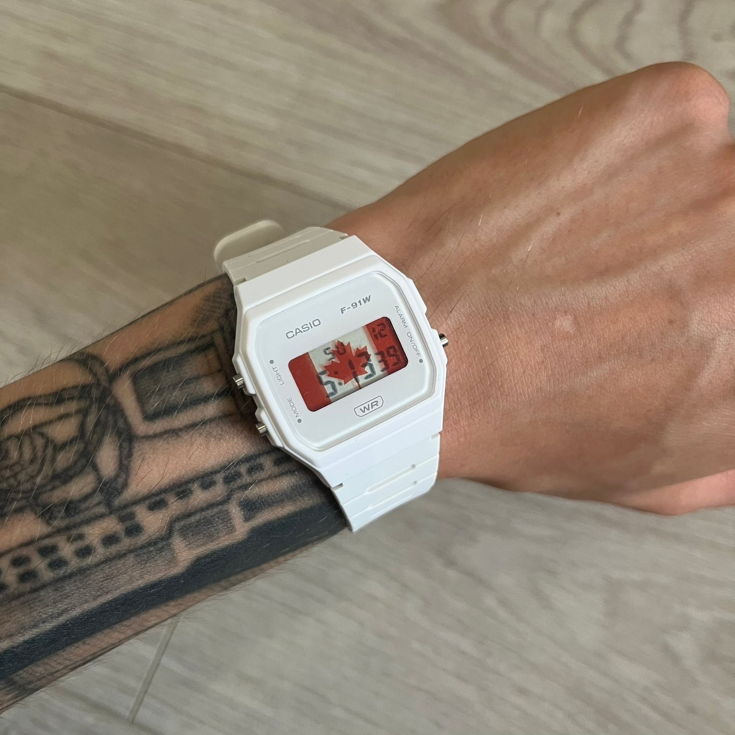 White Casio watch on a wrist with a tattooed arm, on a neutral background