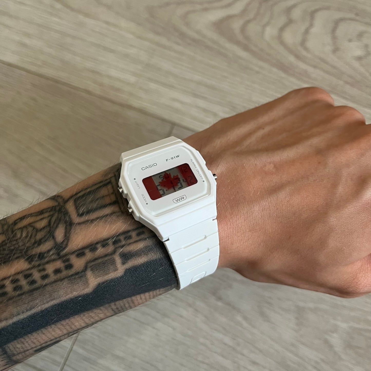 White Casio digital watch on a wrist with tattoos against a wooden background