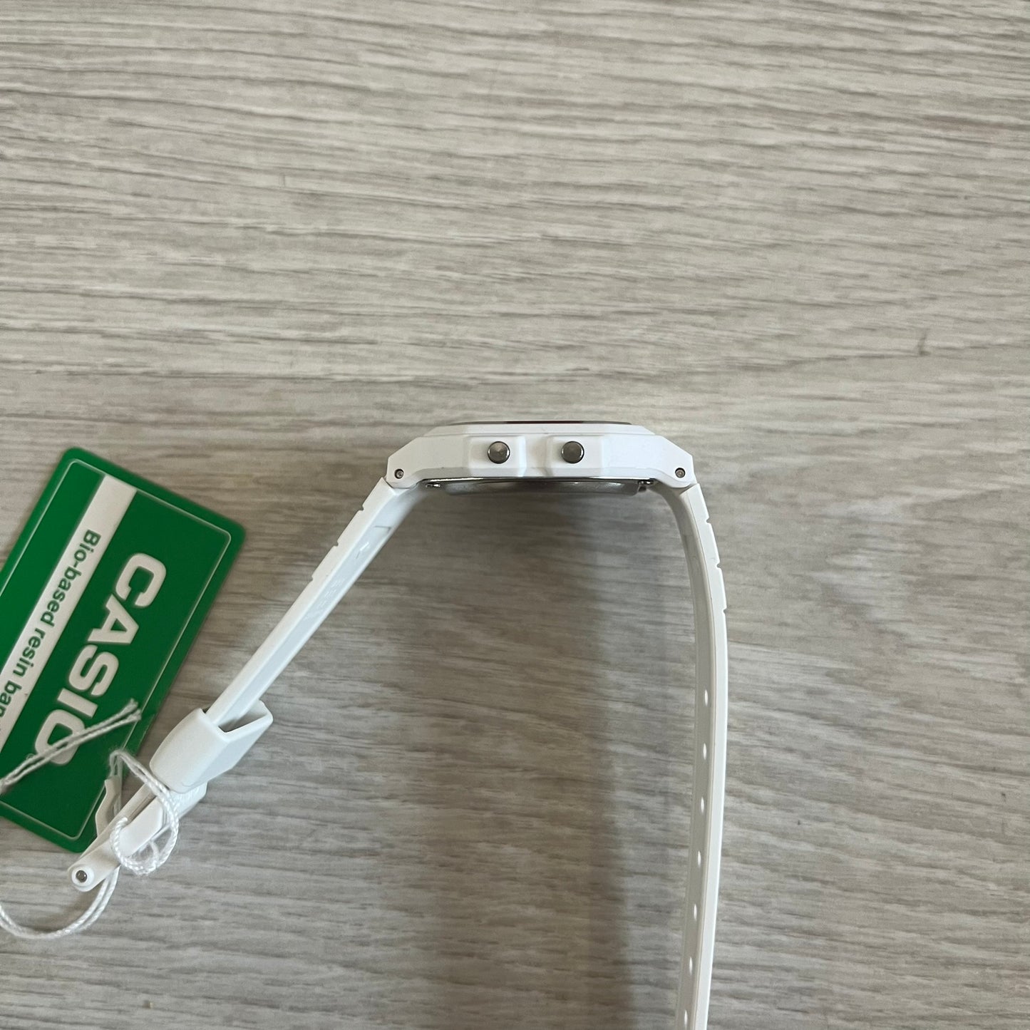 White Casio watch strap on a wooden surface with a green Casio tag.