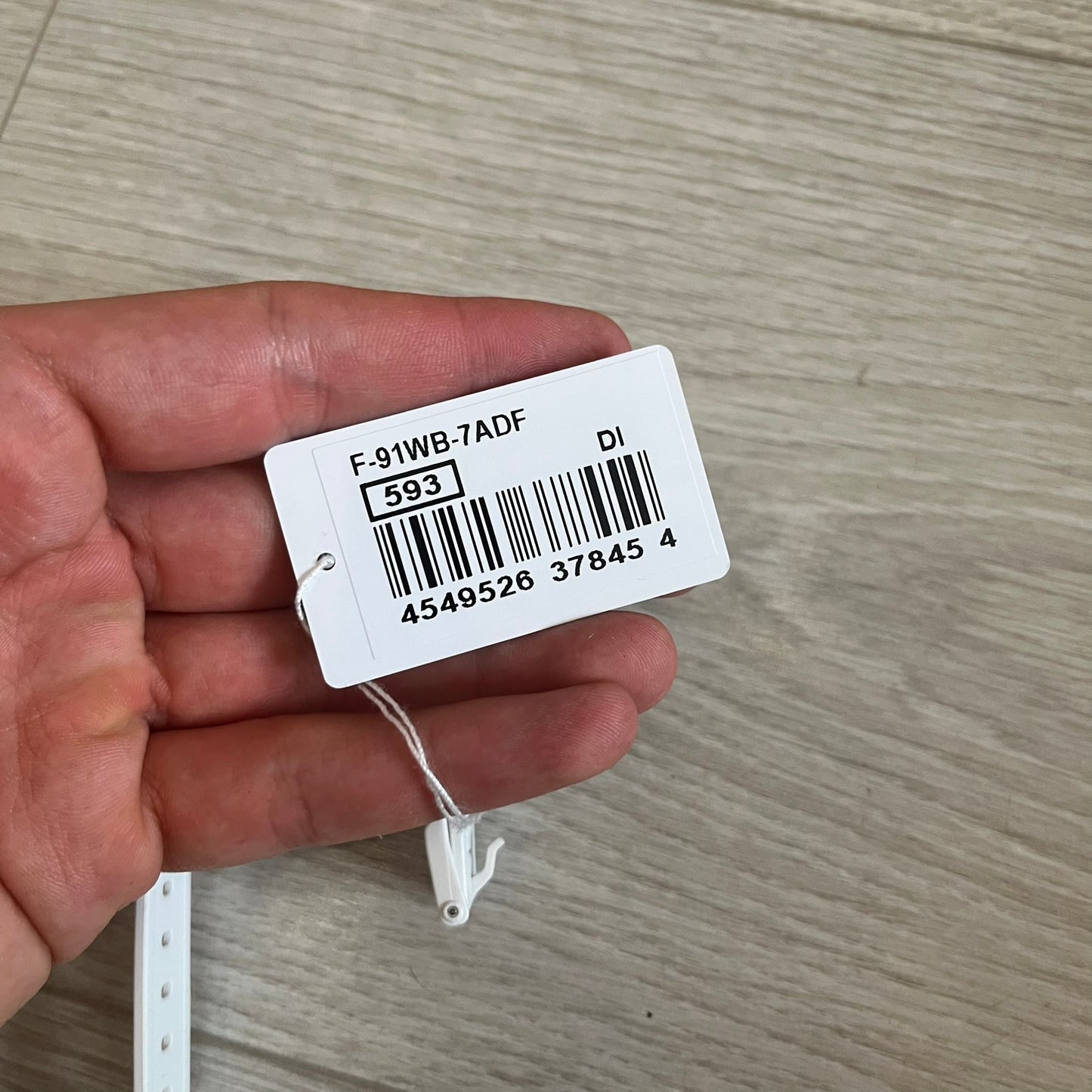 Hand holding a product tag with a barcode and text on a wooden surface