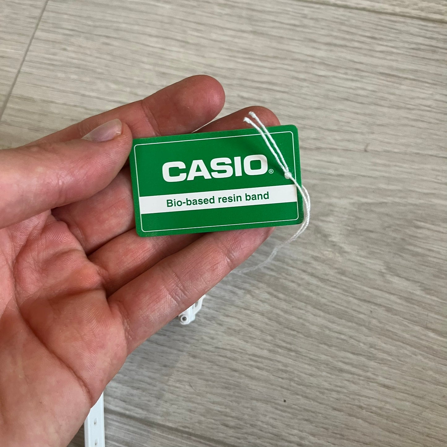 Hand holding a Casio bio-based resin band tag on a wooden surface