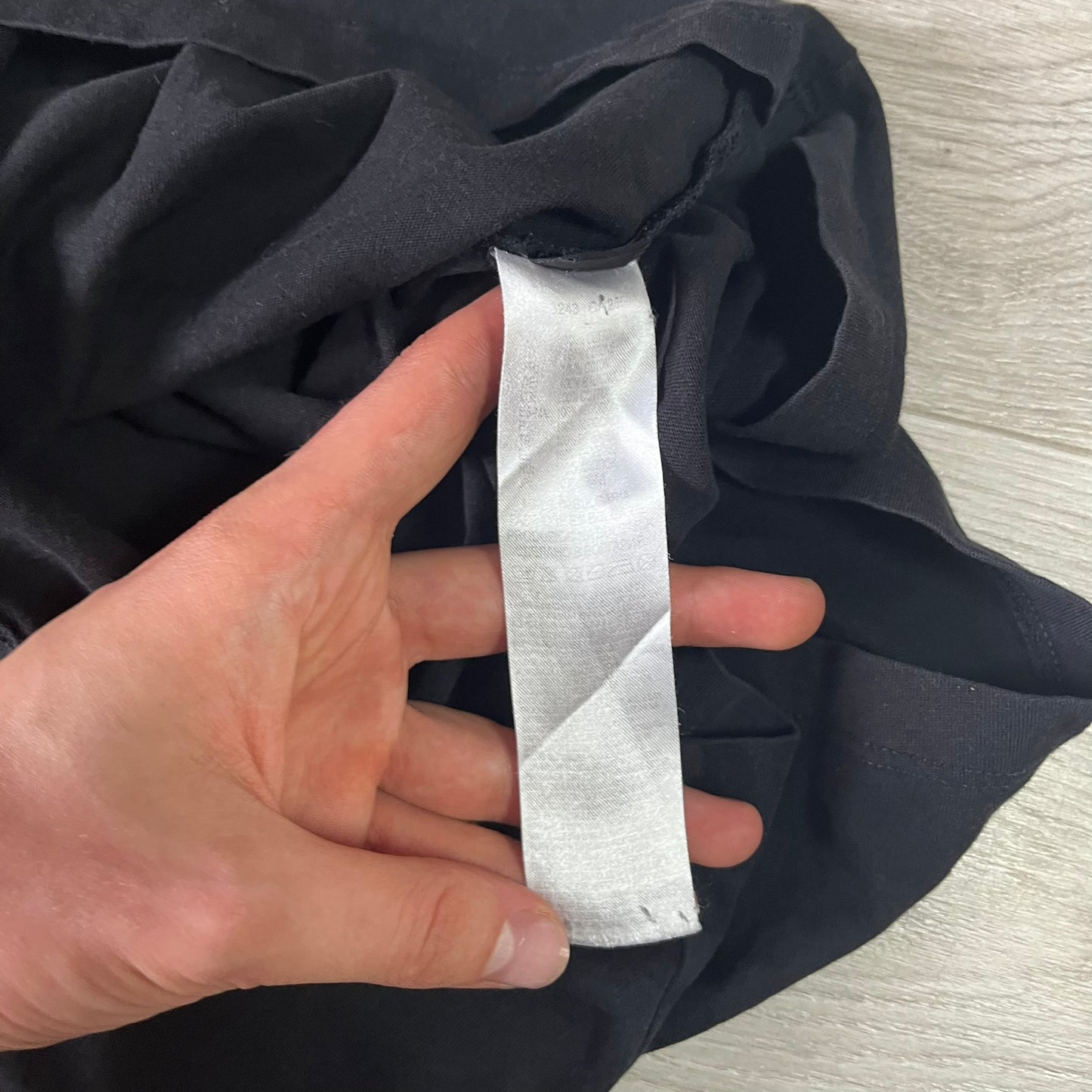 Hand holding a strip of white fabric against dark fabric on a light wooden surface