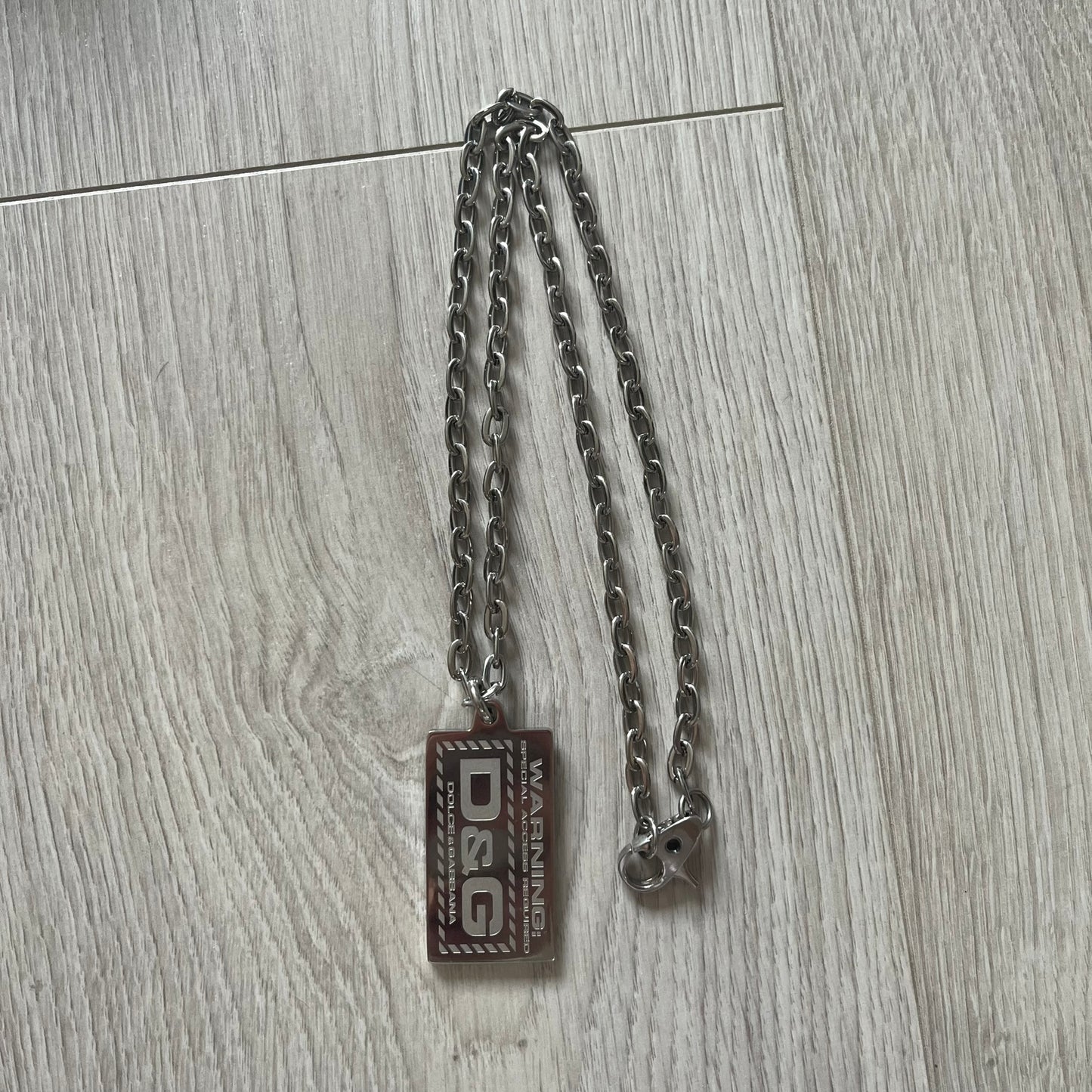 Silver chain with a rectangular tag on a wooden surface