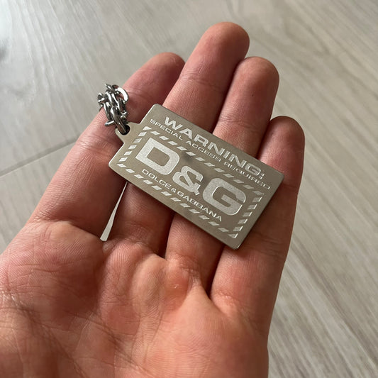 Hand holding a silver 'D&G' tag against a light background