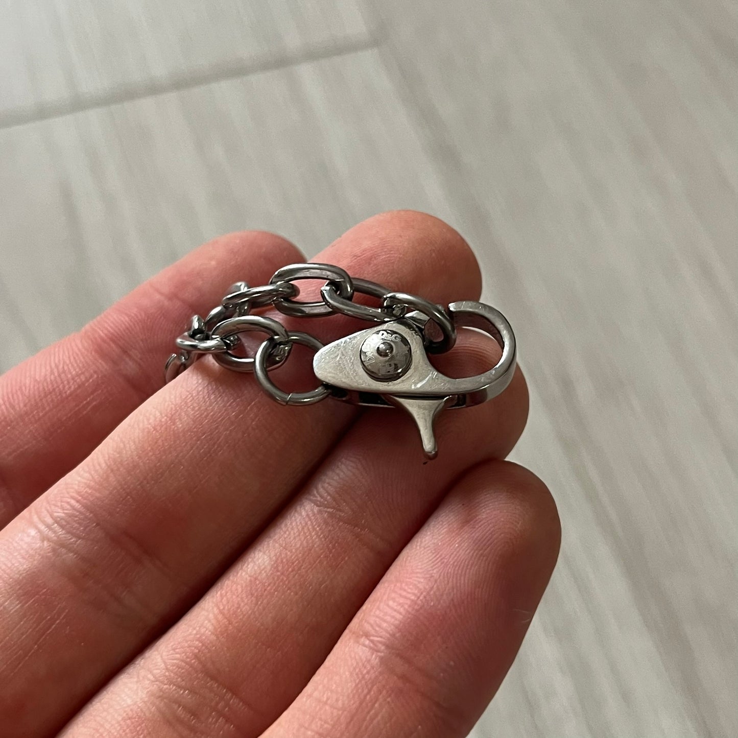 Hand holding a silver chain bracelet with a clasp on a light background