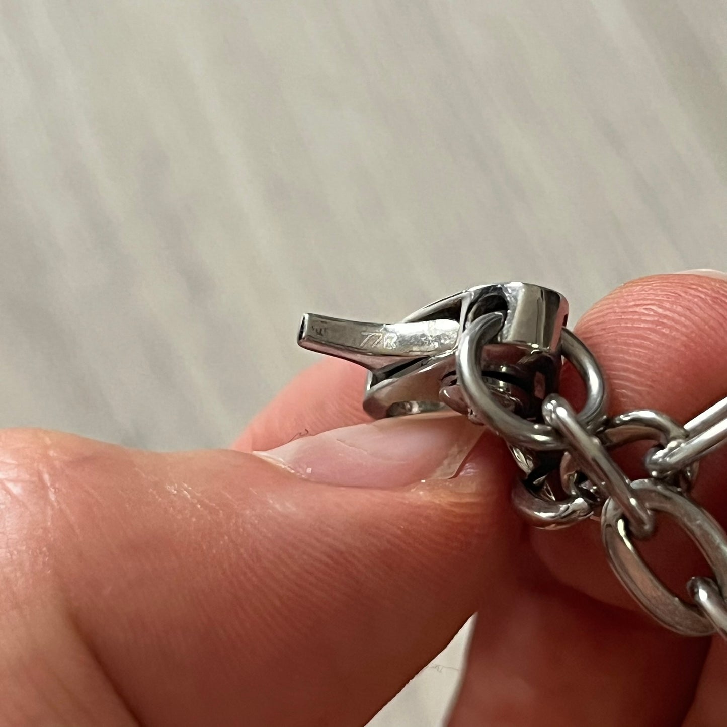 Close-up of a silver chain with a clasp held between fingers on a neutral background