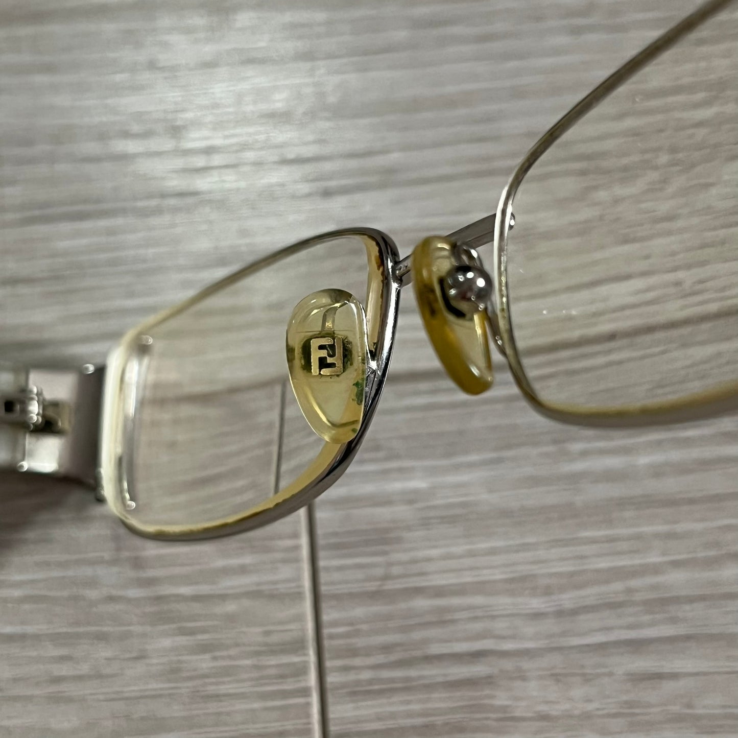 Gold-framed eyeglasses with a logo on a wooden surface