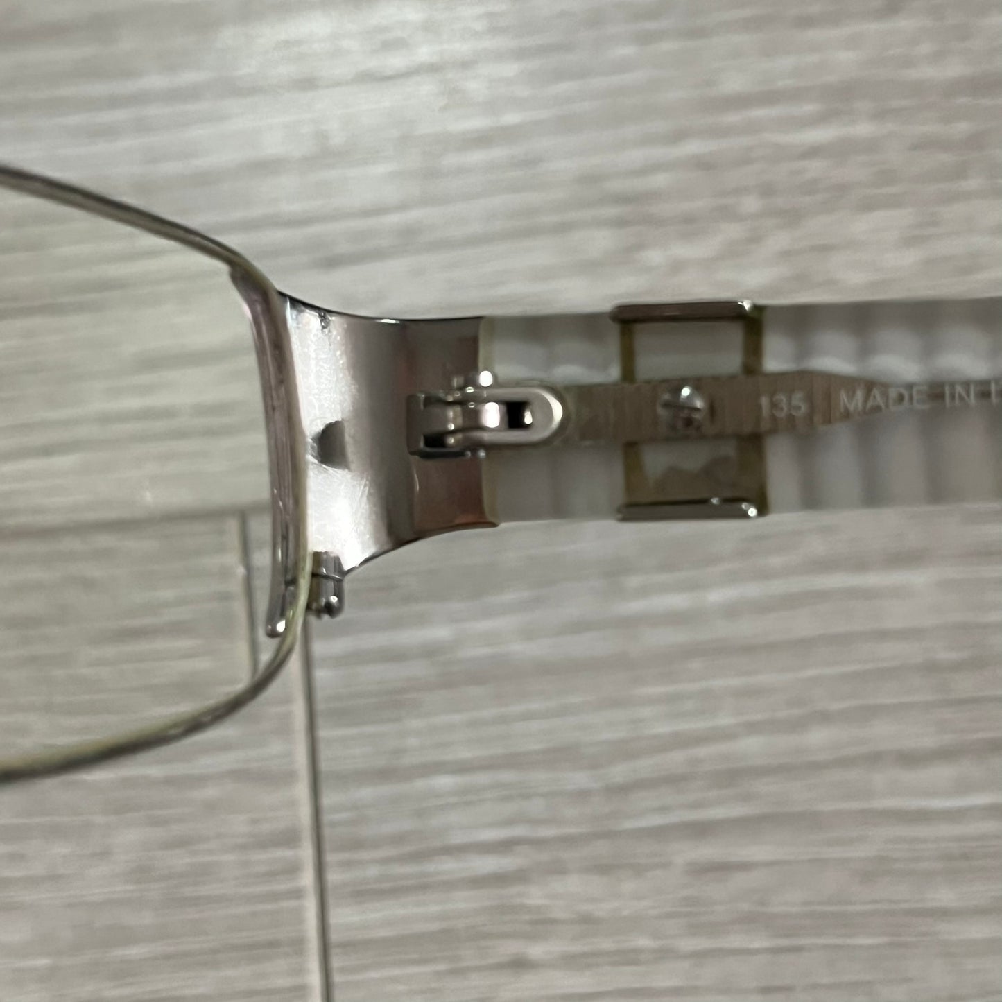 Close-up of a silver eyeglass frame on a textured gray background