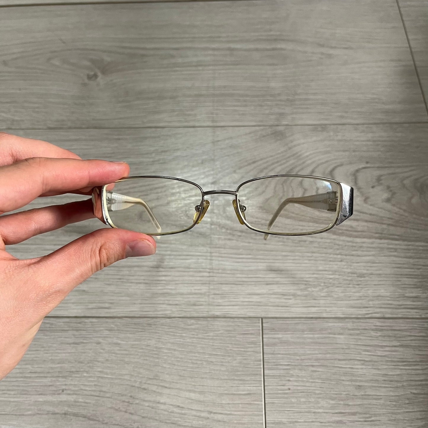 Hand holding a pair of glasses on a wooden floor