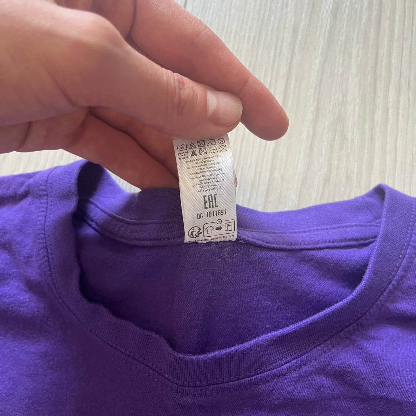 Purple shirt with a tag held by a hand on a light background