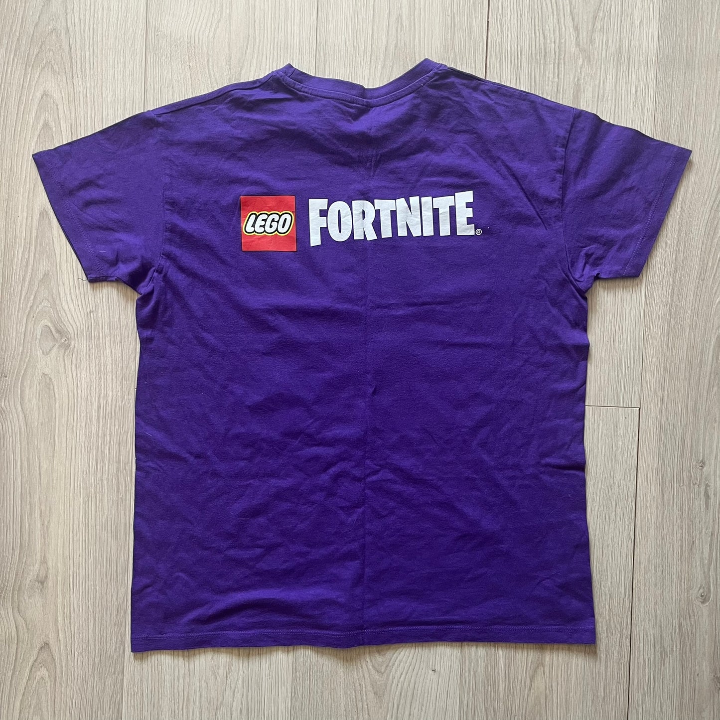 Purple t-shirt with LEGO Fortnite logo on a wooden floor