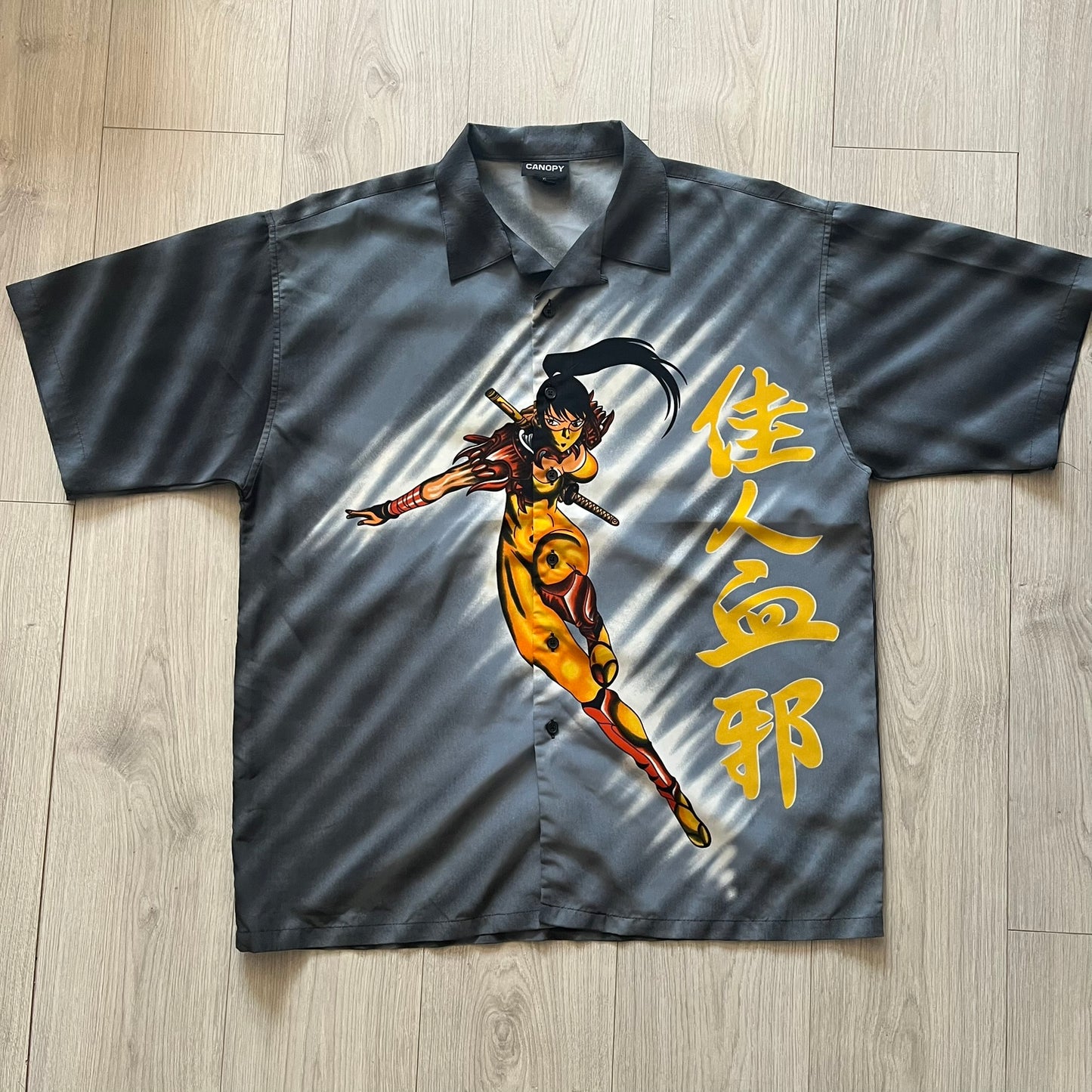Gray shirt with a colorful graphic of a warrior and Chinese characters on a wooden floor.