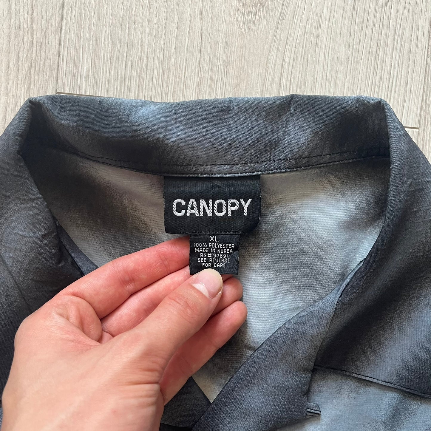 Hand holding a 'CANOPY' label on a piece of gray fabric.