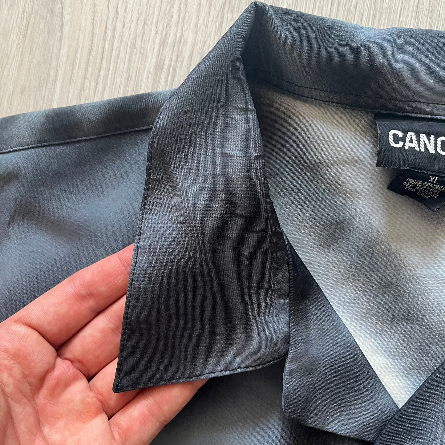 Gray fabric with a visible brand label held by a hand on a light wooden surface.