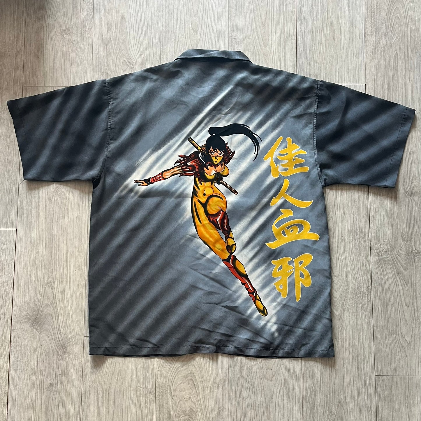 Gray shirt with a colorful graphic of a warrior and Japanese text on a wooden floor.