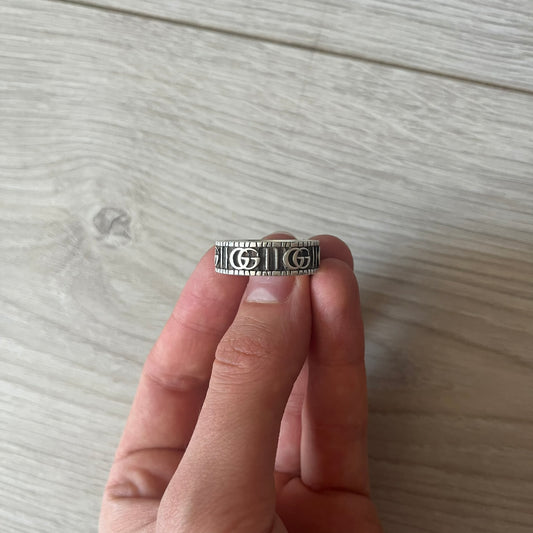 Silver ring with a pattern worn on a finger against a light wooden background