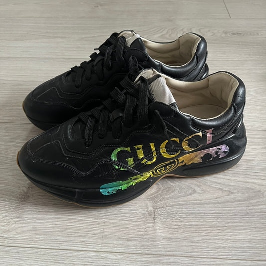 Black Gucci sneakers with floral design on a wooden floor