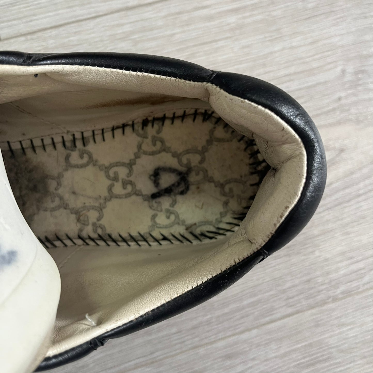 Close-up of a shoe's interior lining with decorative stitching on a light wooden surface.