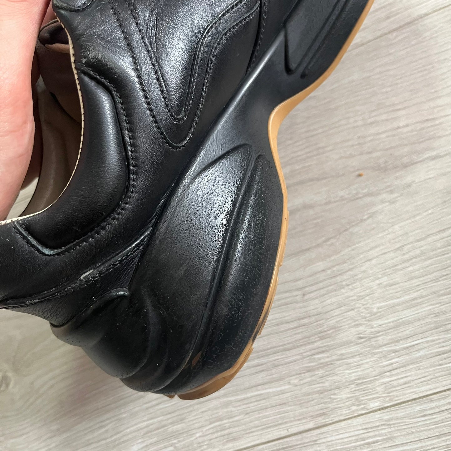 Black leather shoe with a brown sole on a light wooden floor